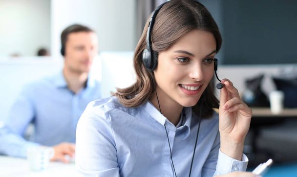 Portrait of call center worker accompanied by his team. Smiling customer support operator at work. - 写真・画像