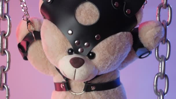 Teddy bear suspended from chains in bdsm accessories in neon light in smoke - Footage, Video