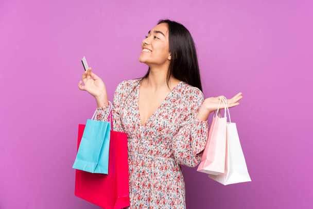 Young Indian woman isolated on purple background holding shopping bags and a credit card - Foto, Imagen