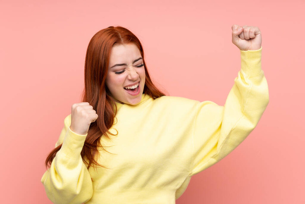 Rotschopf Teenager Mädchen über isoliertem rosa Hintergrund feiert einen Sieg - Foto, Bild