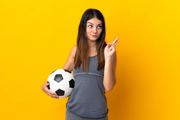 Молодая футболистка изолирована на желтом фоне со скрещиванием пальцев и желанием всего наилучшего - Фото, изображение