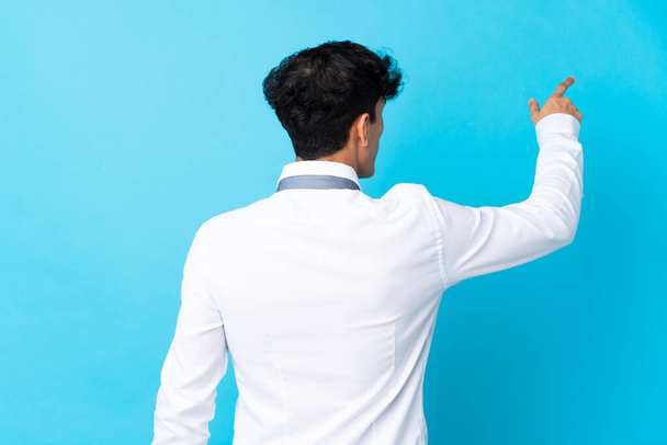Молодий аргентинський бізнесмен над ізольованим синім фоном вказує назад вказівним пальцем. - Фото, зображення