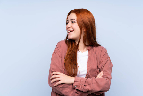 Redhead teenager dívka přes izolované modré pozadí šťastný a usmívající se - Fotografie, Obrázek