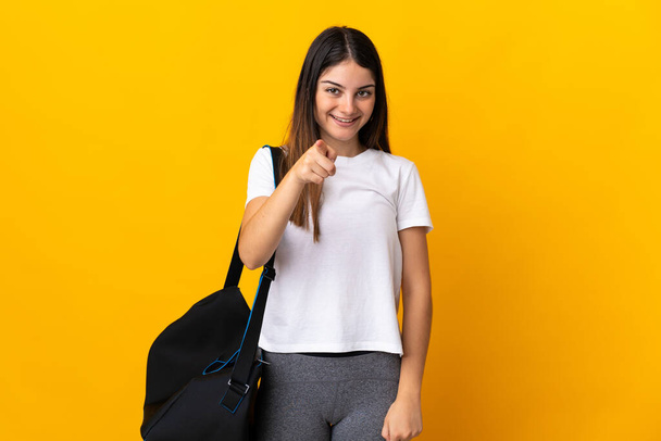 Young sport woman with sport bag isolated on yellow background surprised and pointing front - Valokuva, kuva