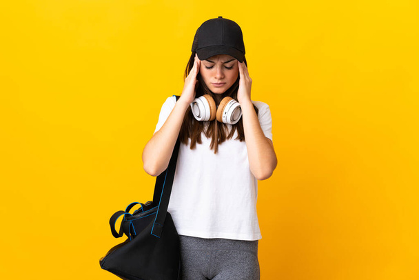Молодая спортивная женщина со спортивной сумкой на желтом фоне с головной болью - Фото, изображение