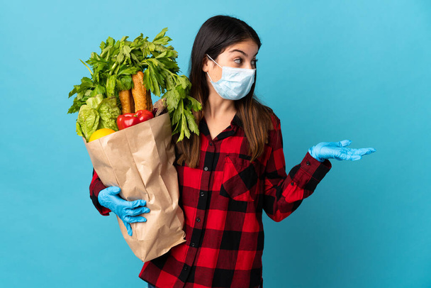 Fiatal kaukázusi zöldségek és maszk elszigetelt kék háttér meglepetés arckifejezés - Fotó, kép