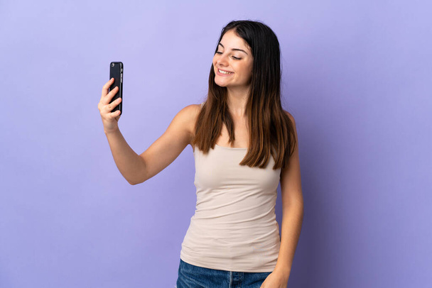 jonge Kaukasische vrouw geïsoleerd op paarse achtergrond het maken van een selfie - Foto, afbeelding