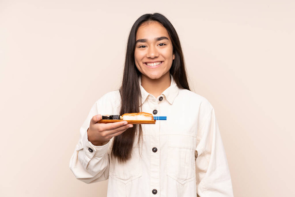 Mladá indická žena drží sushi izolované na béžové pozadí s úsměvem hodně - Fotografie, Obrázek