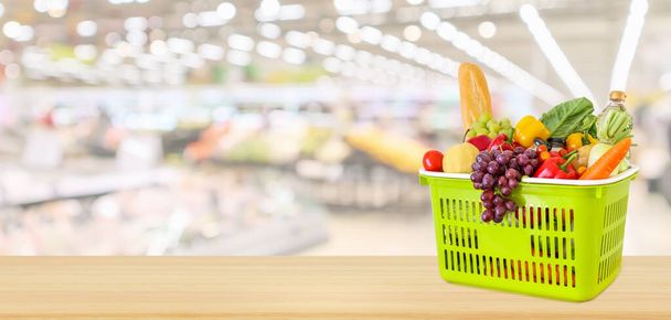 スーパーマーケットのある木のテーブルの上に果物や野菜でいっぱいのショッピングバスケットぼやけた焦点を当てたパノラマの背景 - 写真・画像