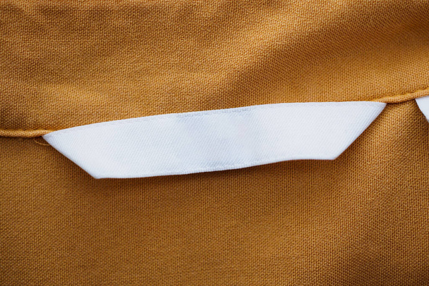 Bianco etichetta di abbigliamento bianco su sfondo camicia marrone - Foto, immagini