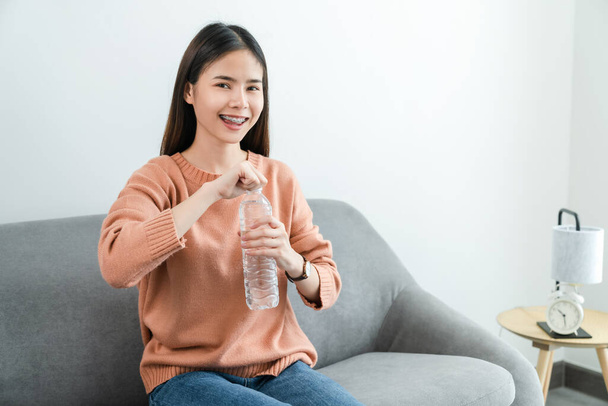 Молода азіатка тримає пляшку з водою і на дивані вдома.. - Фото, зображення