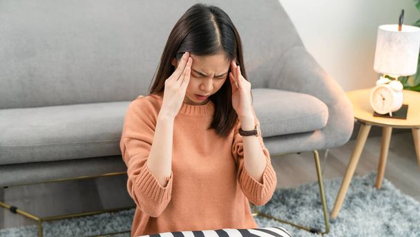 Moe jonge Aziatische vrouw zitten en hebben een hoofdpijn omdat migraine. - Foto, afbeelding