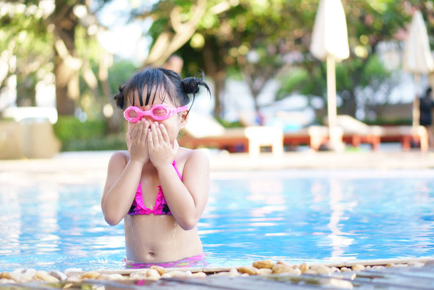 Asian child cute or kid girl wear pink bikini and goggles for swimming and choke water with happy fun on swimming pool or water park and nature for refreshing and relax with exercise on summer holiday - Foto, Imagem