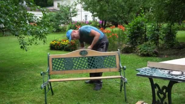 Jardinero hombre desmontar banco retro en jardín patio. Renovación de mobiliario exterior - Imágenes, Vídeo