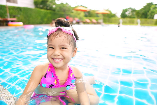 Asian children cute or kid girl wear pink bikini and goggles on swimming pool or water park and smile with enjoy happy or funny for refreshing and relax exercise on summer holiday and vacation - Photo, Image