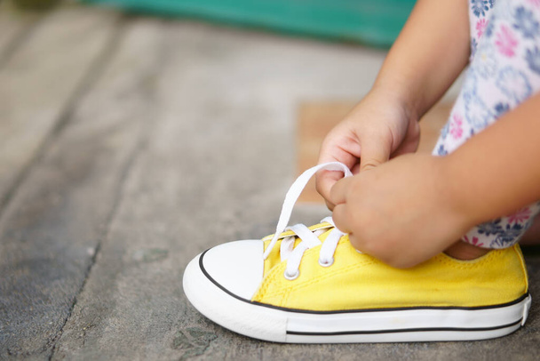 kéz a gyermekek vagy a gyerek lány tanulás és próbálja meg nyakkendő cipőfűző sárga cipő vagy tornacipő kötél és lábbeli séta utazás és divat az utcán, független és ingyenes - Fotó, kép
