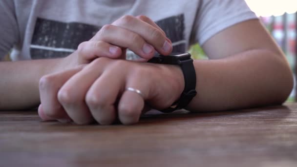 mężczyzna siedzi przy stole na ulicy i używa inteligentnego zegarka - Materiał filmowy, wideo