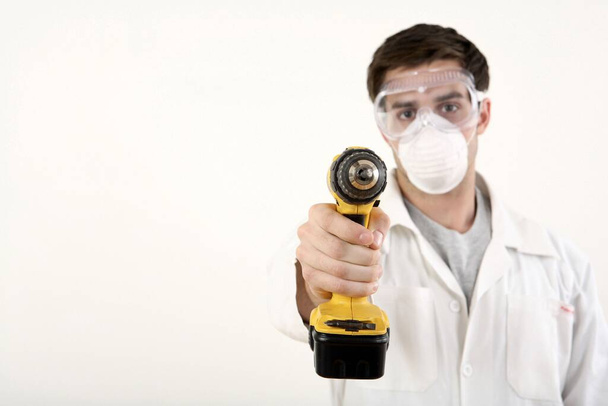 Man with safety mask and goggles pointing a power drill at the camera - Fotoğraf, Görsel