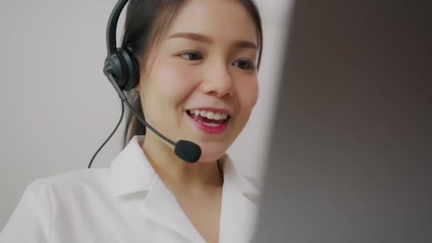 Uśmiechnięta azjatycka konsultantka biznesowa nosząca mikrofon słuchawkowy operatora telefonu obsługi klienta w miejscu pracy. - Materiał filmowy, wideo