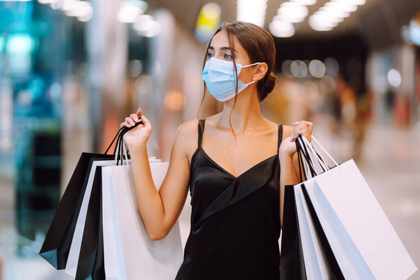 Woman in shopping. Young woman in protective sterile medical mask on her face with shopping bags in the mall. Purchases, black friday, discounts,  sale concept. Covid-2019. - Fotografie, Obrázek