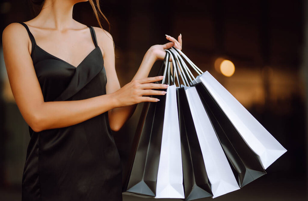 Shopping bags of women crazy shopaholic. Fashionable woman dressed in a black dress  with shopping bags. Purchases, black Friday, sale concept. - 写真・画像