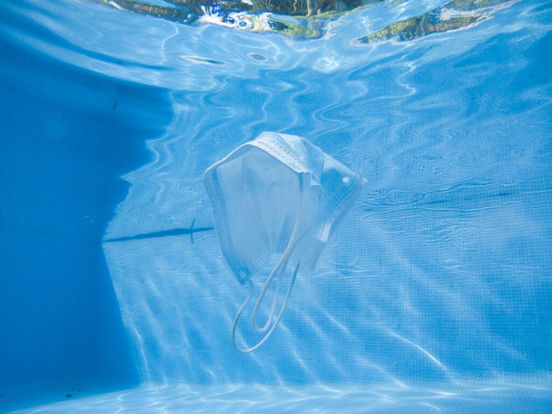 Un primer plano de una mascarilla protectora ahogada en el agua de una piscina - Foto, imagen