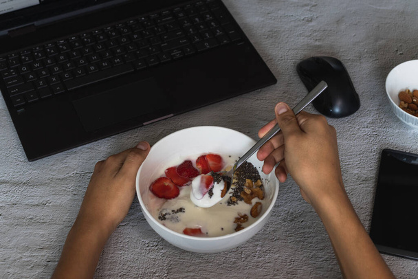 Egy nagy szög lövés egy személy eszik joghurt gyümölcsökkel használata közben a laptop - Fotó, kép