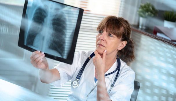 Médico femenino examinando informe de rayos X en consultorio médico; efecto de luz - Foto, imagen