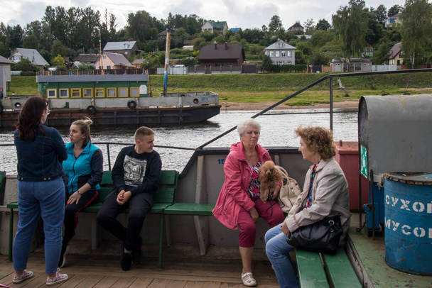Tutaev, Russia - July 16, 2029 Volga landscape with a high opposite shore with a white church. People on the ferry at the side of the ferry across the wide river in the foreground - Photo, Image