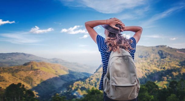 Young curly female traveler with a backpack and in a hat admiring enjoying the beautiful mountain landscape, travel and freedom lifestyle - Foto, Imagen