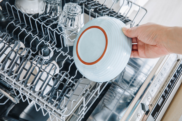 Gros plan sur la machine à laver le lave-vaisselle. Femme main sortant plat propre après le lavage. - Photo, image
