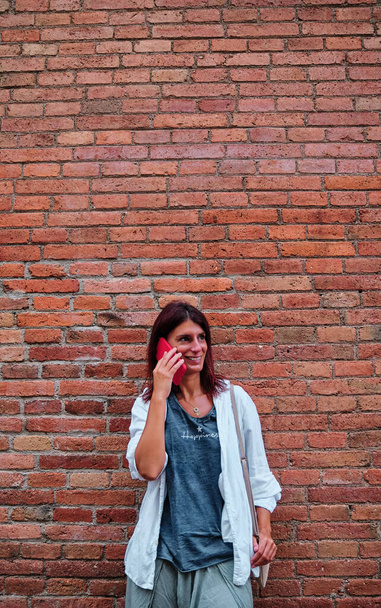 adult woman using mobile phone with brick wall behind - Fotoğraf, Görsel