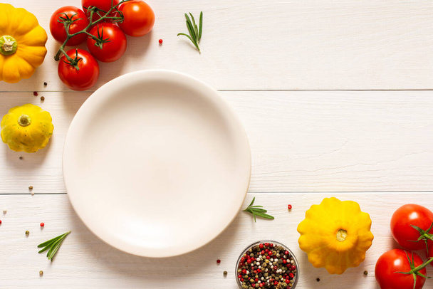 Fondo de madera blanca con plato vacío e ingredientes, tomates y romero, calabaza pattypan y especias, vista superior - Foto, Imagen
