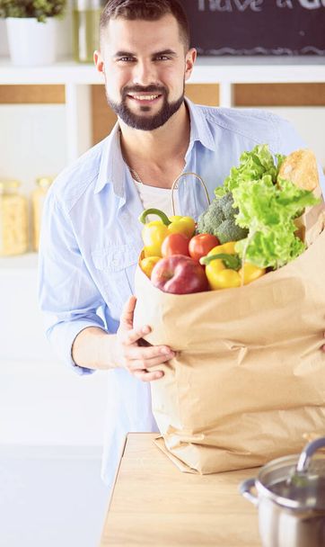 Man holding paper bag full of groceries on the kitchen background. Shopping and healthy food concept - Foto, afbeelding