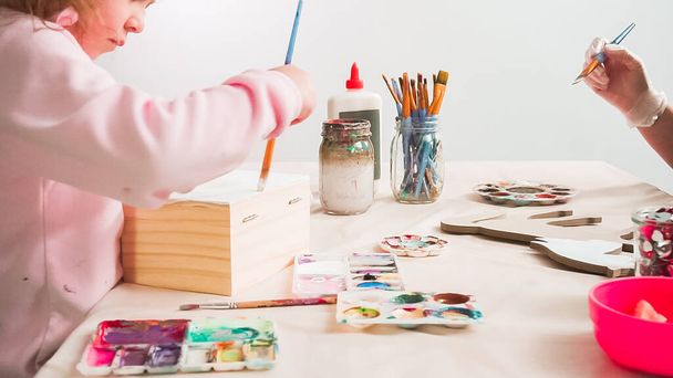 Маленька дівчинка малює білий єдиноріг акриловою фарбою на дерев'яній коробці
. - Фото, зображення