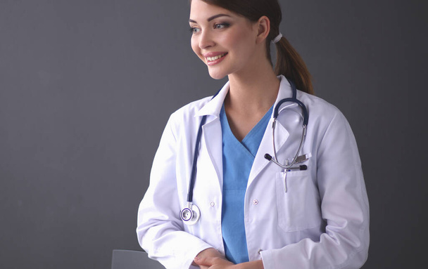 Beautiful female doctor standing near stool isolated grey background - Photo, Image