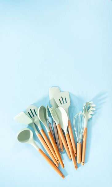 Flat lay. New blue silicone kitchen utensils with wooden handles on a blue background. - Photo, Image
