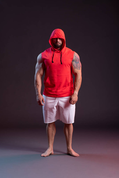 Powerful muscular man with a hood posing in the red sweatshirt. - Foto, Imagen