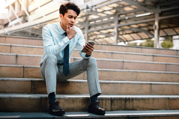 Young Striving Asian Businessman Using Mobile Phone in the City. Sitting on Staircase. Reading Seriously topic via Smartphone - Foto, Imagem