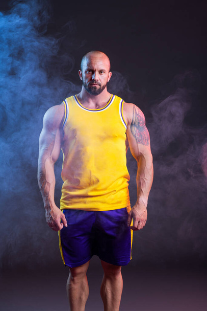 Powerful muscular man posing in the studio with red and blue smoke - Fotoğraf, Görsel