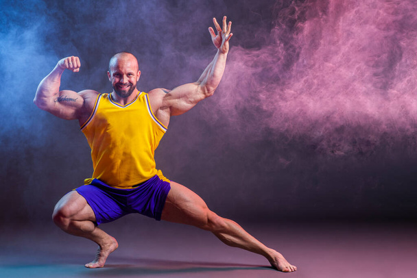 Powerful muscular man posing in the studio with red and blue smoke, Biceps and leg contraction - Foto, Imagem
