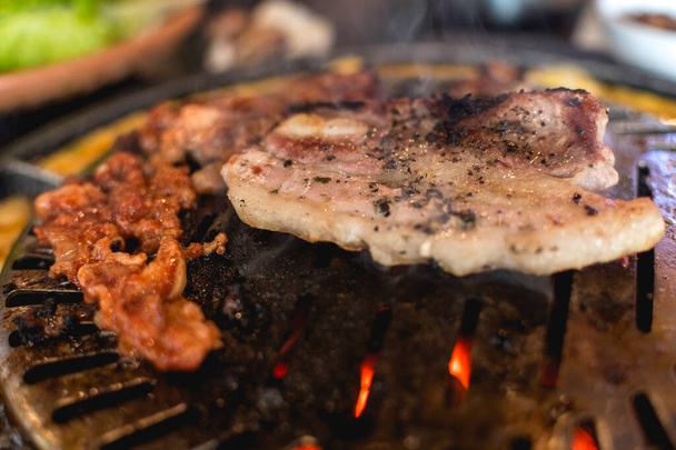 Closeup of marinated beef strips and pork belly on a hot round grill. Samgyeopsal or Korean cuisine. - Photo, Image