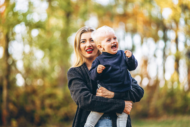 Happy mother with her little baby son have fun in the city park with colorful leaves around in autumn time. Happy family and mothers day concept - Фото, зображення