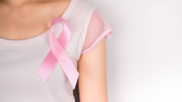 Ροζ κορδέλα στο αριστερό στήθος της γυναίκας φορώντας ένα λευκό t-shirt με λευκό φόντο, το σύμβολο του καρκίνου του μαστού, το μήνα ευαισθητοποίησης του καρκίνου του μαστού. Σημαντικές ημέρες του Οκτωβρίου - Φωτογραφία, εικόνα