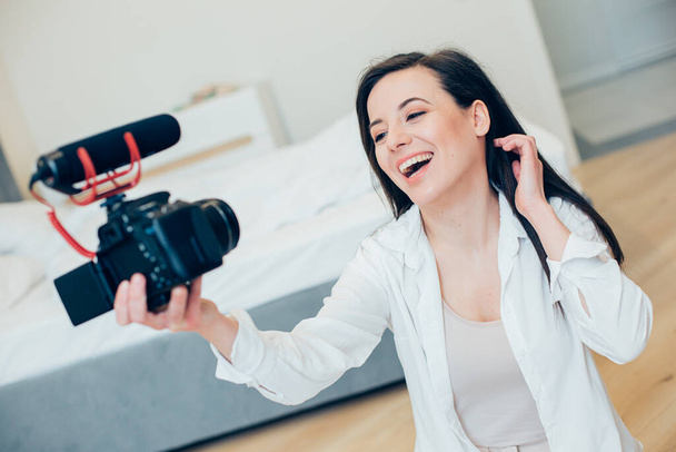 Pleased young lady posing on a camera while recording a video of herself at home - Foto, Imagem