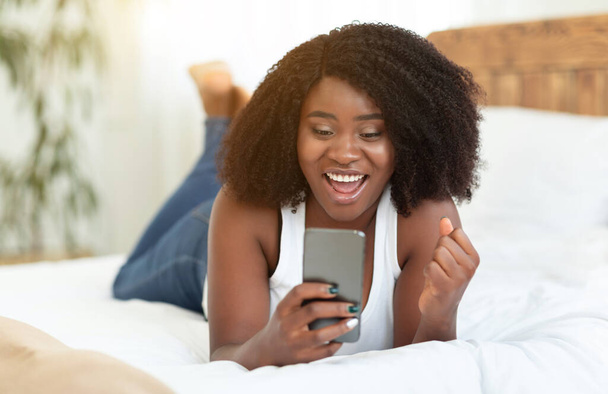 opgewonden afro meisje gevoel extatische holding telefoon - Foto, afbeelding