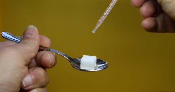 een klontje suiker op een lepel wordt besprenkeld met medicijnen uit een pipet - Video
