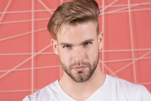 Man with bristle on strict concentrated face, pink background. Masculinity concept. Man with beard or unshaven guy looks handsome and well groomed. Guy bearded and attractive with hairstyle - Photo, image