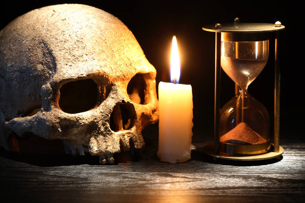 Vintage νεκρή φύση με κερί φωτισμού κοντά στο ανθρώπινο κρανίο και κλεψύδρα - Φωτογραφία, εικόνα