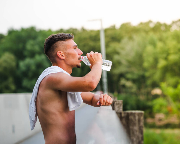 Молодой привлекательный спортсмен питьевой воды после тренировки - спортивная концепция - Фото, изображение